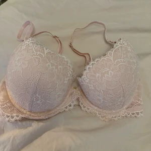 BH - Säljer en ljusrosa bh från H&M i storlek 75C med vacker spets och blommigt mönster. Bh:n har justerbara axelband, dekorativ spetskant och en liten guldfärgad detalj mellan kuporna. Materialet är polyamid, elastan och polyester.