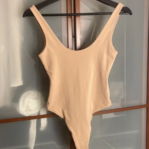 Beige body  - Snygg beige body från Bik Bok i storlek XS. Modellen har djup urringning både fram och bak, breda axelband och en enkel, stilren look.
