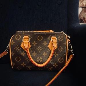 Louis Vuitton liknande väska  - Säljer en ikonisk Lv handväska i brunt skinn med klassiskt LV-mönster och beige detaljer. Väskan har både handtag och axelrem, samt dragkedja i guld. Perfekt storlek för det viktigaste och en riktig statement piece.