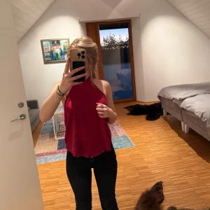 Röd omlott linnetopp med knyt - Säljer en snygg röd linnetopp med omlott-design och breda band som knyts i nacken. Toppen är ärmlös och har öppen rygg. Materialet är mjukt och har en lätt glans. Passar dig som gillar att visa lite rygg. aldrig använd förut.