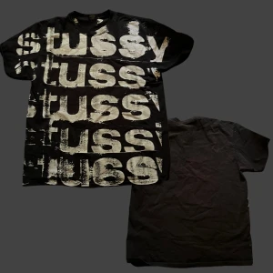 Svart Stussy t-shirt med stor logga - Svart t-shirt från Stussy i storlek L med stort, vittryckt Stussy-logga i flera rader över hela framsidan. T-shirten har klassisk passform, rund hals och korta ärmar. Materialet är mjuk bomull och trycket har en cool, sliten effekt. Perfekt skick. Rare stussy.