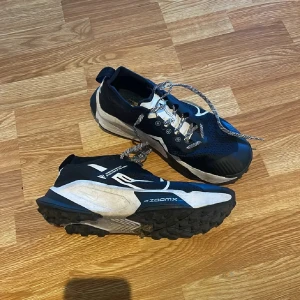 Nike ZoomX Zegama Trail sneakers - Nike ZoomX Zegama Trail sneakers i svart och vitt med grov sula för extra grepp. Ovandelen är ventilerande mesh med vita detaljer och snörning. Perfekta för dig som gillar att springa i terräng och vill ha stabilitet och komfort. Snygg, sportig look med coola kontraster. Kostar nya över 2000kr