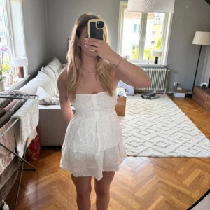 Anglaisestickad bandeau-miniklänning - Anglaisestickad bandeau-miniklänning från NAKD i storlek 34. Endast använd en gång. Har en dragkedja på sidan (se bild) samt en inre silikonkant på brösten och en knappdetalj längs framsidan. Org pris: 549kr #bandeau #bandeudress #sommarkläder #sommarklänning #vitklänning #kortklänning #miniklänning