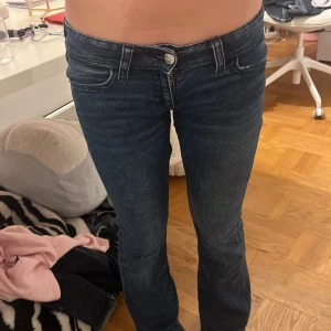 Mörkblå bootcut jeans med snygga fickor - Mörkblå jeans från Gina Tricot med bootcut-modell och låg midja. Jeansen har klassisk femficksdesign, snygga detaljerade bakfickor med knapp och slitningar för en cool look. Perfekta om du gillar en lite retro vibe och vill ha jeans som sitter tajt upptill och släpper vid benen.