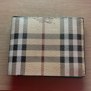 Burrbery plånbok  - Snygg plånbok från Burberry med klassiskt rutig design i beige, svart och rött. Utsidan har en lyxig struktur och insidan är svart med plats för kort. Perfekt för dig som vill ha en stilren och ikonisk accessoar i fickan.