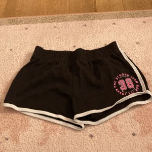 Svarta sportshorts från H&M⛹️‍♀️⛹️‍♀️⛹️‍♀️✨✨✨ - Svarta sportiga shorts från H&M med vit kant och resår i midjan. Tryck på ena benet med siffran 36 och text i rosa. Perfekta för träning eller chill dagar. Mjukt bomullsmaterial som är skönt mot huden VARNING: 🚨väldig trendig och snygg, risk att bli bländad! 🚨🤩🤩🤩