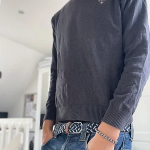 Svart v-ringad tröja från Gant - Svart v-ringad tröja från Gant med diskret logga på bröstet. Tröjan har ribbade muddar vid ärmslut och nederkant, och är tillverkad i mjukt bomullsmaterial. Perfekt för lager-på-lager och funkar året runt.