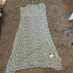 Blommig blå långklänning från SHEIN - Supersöt långklänning från SHEIN med smala axelband och blåvitt blommönster. Klänningen har en rak passform och är tillverkad i lätt polyester, perfekt för varma dagar. Snygg och enkel att styla med sneakers eller sandaler.