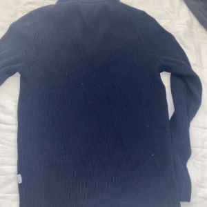 Marinblå stickad half zip från Jack & Jones - Säljer en marinblå stickad tröja från Jack & Jones i storlek XS. Tröjan har ribbad struktur, lång ärm och en snygg half zip-dragkedja vid halsen. Perfekt för dig som gillar stilrena och bekväma plagg med en modern touch.