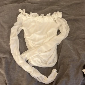Vit mesh blus från Gina Tricot - Supersöt vit blus från Gina Tricot i mesh med långa ärmar och volangdetaljer längs den offshoulder-skurna halsen. Perfekt för dig som gillar romantiska vibes och vill sticka ut lite extra. Säljes i storlek XS.