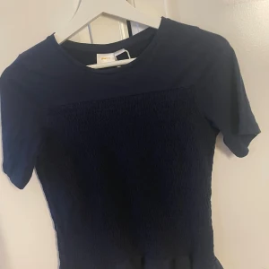 Mörkblå smockad tröja från Gina Tricot - Supersöt mörkblå tröja från Gina Tricot med korta ärmar och smockad midja. Enkel och stilren design Mjuk och skön bomullskänsla, rund halsringning och figurnära passform. Är i 158/164 men passar S-m originalpris 350kr knappt tecken på användning