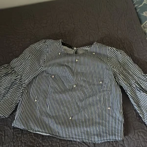 Randig blus med pärlor från Zara XS - Säljer en blåvit randig blus från Zara Basic Collection i storlek XS. Blusen har långa vida ärmar, rund halsringning och är dekorerad med små pärlor framtill. Perfekt för dig som gillar unika detaljer och klassiska ränder.