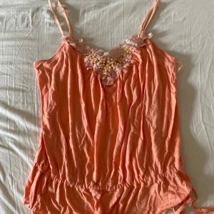 Linnetopp med spets från BAY - Korallfärgat linne från BAY med spets och pärlor. Strl 14 passar en S. Fraktar gärna tillsammans med andra varor.