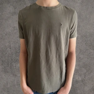 Olivgrön t-shirt från Morris S - Snygg olivgrön t-shirt från Morris med liten broderad logga på bröstet. Klassisk rund hals och korta ärmar. Tillverkad i mjuk bomull som känns skön mot huden. Perfekt för en clean och stilren look.