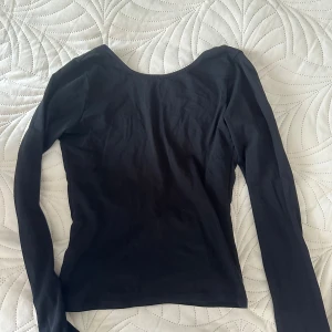 Svart långärmad topp från Nelly - Svart långärmad topp från Nelly med djup, öppen rygg. Snygg och enkel design i stretchigt material som sitter tight mot kroppen. Perfekt för dig som vill ha en basic topp med en twist. Passar till både jeans och kjol.