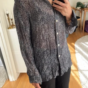Leopardmönstrad skjorta från Helline - Vintage transparent skjorta från Helline med leopardmönster i grått och svart. Skjortan har klassisk krage, knäppning framtill med vita knappar och långa ärmar. Tunt och luftigt material som känns riktigt chill och edgy. Den behave lite kärleken och några stygn. 