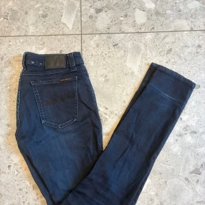 Märkblå nudie jeans - Säljer ett par riktigt feta mörkblå nudie jeans i st 29/32🤩 Byxorna är i fint skick men har fått små vita sträck på benen på både sidorna. Tveka inte på att höra av er vid frågor!🙌🍾