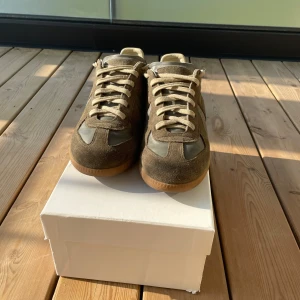 Olivgröna Maison Margiela gats - Snygga Maison Margiala gats i olivgrönt med beige snörning och gummisula. Skorna kommer med orginallådan och dustbags. Säljer för att jag inte använder längre. Bra men använt skick.