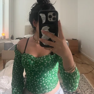 Grön blommig blus med puffärmar - Supersöt grön blus från H&M med vita småblommor, långa puffärmar och smockad rygg. Toppen har en lätt croppad passform och söt rynkning vid bysten. Perfekt för vår och sommar när du vill sticka ut lite extra!