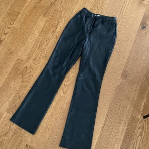 Svarta bootcut byxor i skinn från NA-KD - Snygga svarta byxor från NA-KD i skinnimitation med bootcut-ben och hög midja, storlek 36. De har bälteshällor, sidfickor fram och dekorativa fickor bak. 