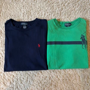 Polo Ralph Lauren 2 tröjor - Två långärmade t-shirts från Polo Ralph Lauren. En är marinblå med röd broderad logga på bröstet, den andra är grön med svart horisontell rand och stor polospelare-tryck. Båda är i mjuk bomull och har klassisk passform. Perfekta för en chill och stilren look.