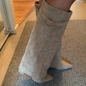 Beige mockastövlar med spetsig tå - Snygga höga stövlar i beige mocka med spetsig tå. Stövlarna har dekorativt spänne i guld och dragkedja på insidan, super fina boots, säljer då dem inte kommer till någon användning, endast användt dem 1 gång. 