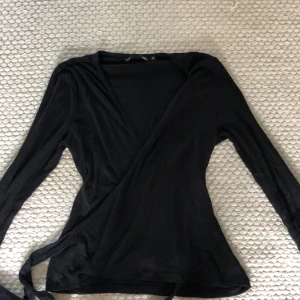 Svart omlottopp - Så snygg svart omlottopp med långa ärmar och knytband i midjan. Säljer för att jag inte använder🥰 Säg till vid minsta fråga!