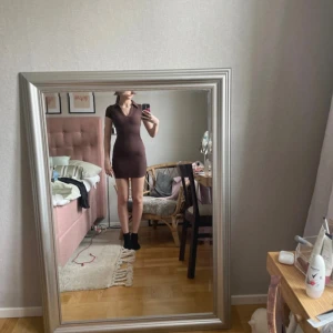 Brun ribbad kortklänning från H&M Divided - Säljer en tight brun kortklänning från H&M Divided i ribbad bomull. Klänningen har v-ringning, korta ärmar och sitter slim på kroppen. Perfekt för dig som gillar en enkel och stilren look med lite edge.