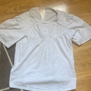 Vit broderad blus från Zara - Superfin vit blus från Zara med broderade detaljer och spets vid bröstet. Blusen har korta ärmar, lätt v-ringning och en luftig passform. Perfekt till sommaren och enkel att matcha med jeans eller kjol.