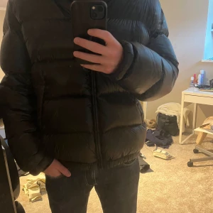 Svart pufferjacka från Zara med huva - Säljer en svart pufferjacka från Zara i storlek L. Jackan har glansig finish, huva och dragkedja framtill. Den är vadderad och har två snedställda fickor. Perfekt för kalla dagar när du vill hålla stilen och värmen. Köpte förra vintern och endast använd under den perioden. 