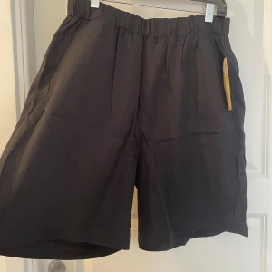 Svarta shorts från Lindex, storlek L - Svarta shorts från Lindex i storlek L. De har en avslappnad passform med resår i midjan och är tillverkade i ett mjukt, lätt tyg som passar perfekt för varma dagar. Klassisk design utan mönster och med diskreta fickor i sidorna.