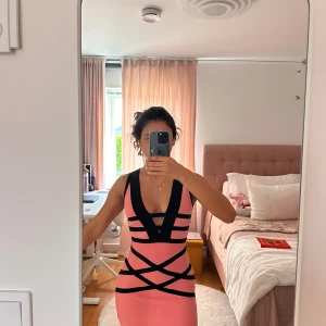 Rosa och svart bandageklänning - Säljer en rosa och svart kort bandageklänning med djup v-ringning och coola svarta banddetaljer. Baksidan har ett rutigt meshmönster och dragkedja. Klänningen är helt oanvänd och figursydd. Skriv för eventuella frågor. Pris kan diskuteras! 🥰