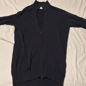 Svart kofta från John Henric - Snygg svart kofta från John Henric med hel dragkedja framtill och ribbade muddar vid krage och nederkant. Perfekt för lager-på-lager och har en stilren look som funkar till många outfits. Materialet känns mjukt och lätt, och koftan har lång ärm. Den är ganska stor i armarna därför säljer jag den. Mycket bra skick fåtals använd. Skriv om du har någon fundering eller bild