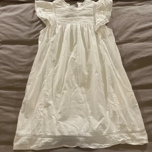 Vit kortklänning från Vintage Stories - Supersöt vit kortklänning från Vintage Stories med volangärmar och broderad överdel. Klänningen har en luftig passform och är perfekt för varma dagar. Snygg och tidlös modell med fina detaljer. Klänning har även fickor en på varje sida 