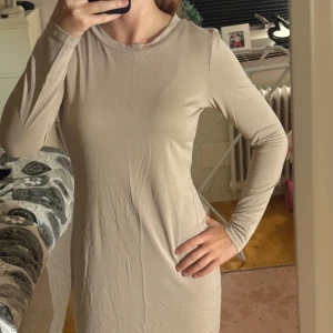 Beige långärmad klänning i bomull - Säljer en enkel och stilren beige klänning med lång ärm och rund hals. Modellen är rak och slimmad, med mjukt och stretchigt bomullsmaterial som sitter skönt mot kroppen. Perfekt för dig som gillar minimalistisk och clean look.