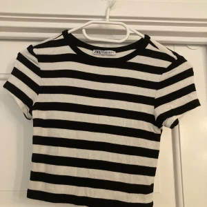 Randig croppad t-shirt från Zara - Snygg croppad t-shirt från Zara med breda svarta och vita ränder. T-shirten har korta ärmar, rund halsringning och är gjord i mjuk bomull. Perfekt för en chill och trendig look. Den är även i mjukt stretchigt material.Kom gärna med förslag på pris. Inte använd och inga fläckar.
