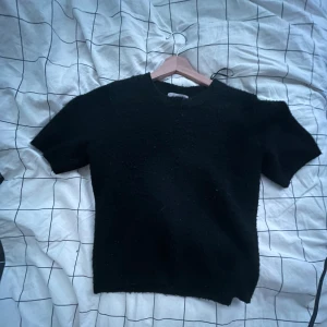 Svart stickad T-shirt - En svart stickad T-shirt från H&M i storlek XS. Tröjan har korta ärmar och en enkel, rak passform med rund halsringning. Perfekt att styla med jeans eller kjol🫶