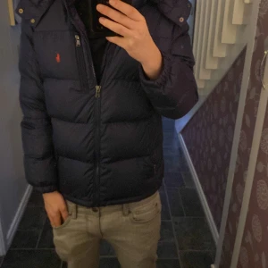 Blå dunjacka från Ralph Lauren - Säljer en blå dunjacka från Ralph Lauren med huva och dragkedja. Jackan har långa ärmar och en liten röd logga på bröstet. Perfekt för kyliga dagar! 💙 Den är storlek 14 till 16 sitter bra på mig som är 171 liten defekt uppe på ryggen men syns inte om man inte har luvan på sig