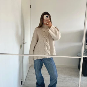 Beige stickad polotröja med fläta - Supermysig beige stickad polotröja med grov fläta framtill. Tröjan har oversized passform, långa ärmar och ribbade muddar. Perfekt för lager på lager och chill höst- och vinterstil.