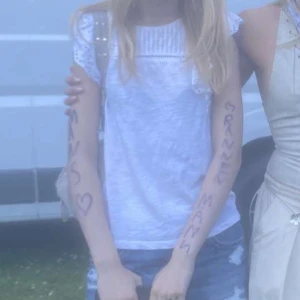 Vit blus med spets - Supersöt vit kortklänning med broderade spetsvolanger på axlarna och ribbad överdel. Klänningen är ärmlös och har en luftig passform, perfekt för varma dagar. Materialet känns som bomull och spetsen ger en romantisk vibe. Passar dig som gillar ljusa och fräscha outfits. Köpt ny för 300kr.