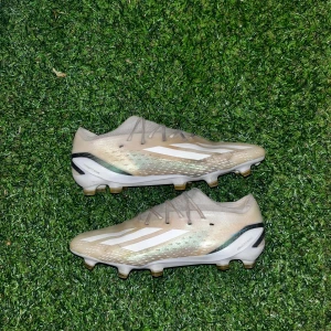 Adidas spelportal.1 - Säljer ett par snygga beige fotbollsskor från adidas med vita och svarta detaljer. Skorna har snörning, låg profil och platt sula med dobbar för gräsplan. Materialet är syntet och designen är sportig med klassiska adidas-ränder på sidan.