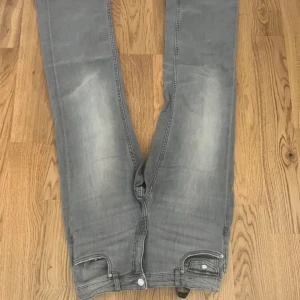 Grå jeansbyxor från Kappahl, stl 164 - Har bara använt ett par gånger. Snygga grå jeansbyxor från Kappahl i storlek 164. Byxorna har raka ben, klassiska fickor fram och bak med lock och knapp, samt slitningar för en cool look. Perfekt för dig som gillar en avslappnad stil.