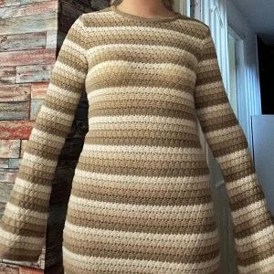 Randig stickad kortklänning veromoda - Supermysig stickad klänning från veromoda  med breda beige och vita ränder. Klänningen är kort, har lång ärm och är gjord i ett virkat stickat material som känns både retro och trendigt. Perfekt för dig som gillar en chill men snygg look.