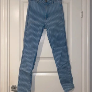Blå randiga jeans med raka ben - Snygga blå jeans med vita vertikala ränder och raka ben. Klassisk femficksmodell med bälteshällor och knappstängning. Jeansen har en fräsch, retroinspirerad look och är tillverkade i robust denim. Perfekta för dig som vill sticka ut lite extra.