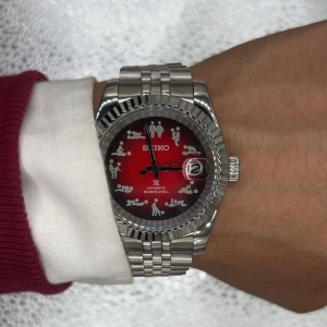 Seiko automatisk dykarklocka röd/silver - Unik Seiko automatisk dykarklocka med röd urtavla och roliga figurer som timmarkeringar. Boett och länk i silverfärgat stål, tydlig datumvisning och robust design. Urtavlan har en cool gradient från rött till svart. 