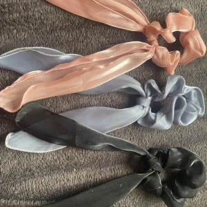 3 scrunchies🤍 - Tre snygga scrunchies i glansigt tyg med långa band, perfekta för att piffa upp din frisyr. En i ljusrosa, en i ljusblå och en i svart. Ger en trendig och feminin look till håret. 30kr styck eller 80kr för alla🫶🏻