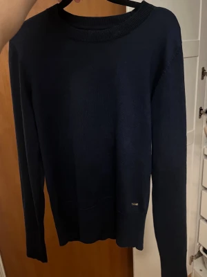 Mörkblå stickad tröja Holly & Whyte - Snygg mörkblå stickad tröja från Holly & Whyte by Lindex. Tröjan har långa ärmar och guldfärgade knappar vid ärmsluten som ger en extra touch. Klassisk rund halsringning och mjukt material som sitter skönt på kroppen. Använd ett fåtal gånger och inga tecken på användning🩷🩷