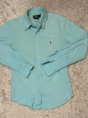 Ljusblå skjorta Polo Ralph Lauren M - Säljer en ljusblå skjorta från Polo Ralph Lauren i slim fit. Klassisk modell med knappar framtill och broderad logga på bröstet. Skjortan har lång ärm och är tillverkad i mjuk bomull. Perfekt till jeans eller chinos.