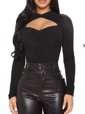 Svart långärmad bodysuit Fashion Nova - Säljer en svart långärmad bodysuit från Fashion Nova med twistad detalj vid halsen och snygg cut-out över bröstet. Tillverkad i mjukt stretchigt material för en åtsittande passform.