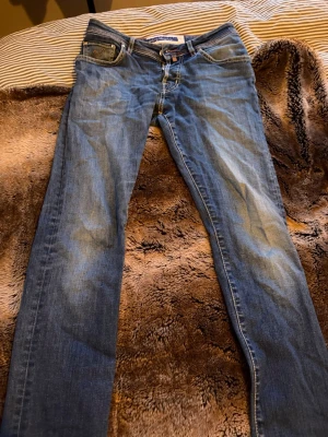 Blå jeans från Jacob Cohen - Säljer ett par klassiska blå jeans från Jacob Cohen med snygg tvätt och raka ben. Jeansen har fem fickor, läderpatch med logga bak och kontrastsömmar. Perfekta till en avslappnad stil och tillverkade i mjukt bomullsmaterial. Jeansen sitter i storleken som ett par 30/32.